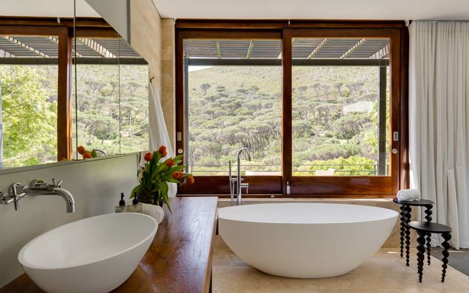 Freestanding bathtub in a luxury Cape Town villa bathroom with panoramic forest and mountain views.