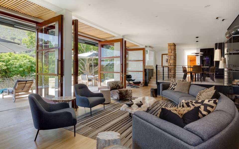 Stylish open-plan lounge at a luxury Cape Town villa with folding doors leading to a sunlit patio and pool.