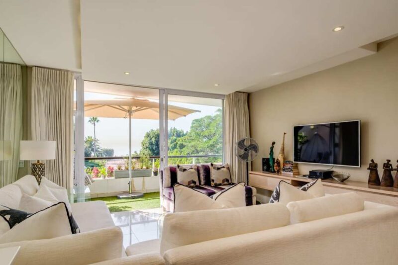 Amani Views bright open-plan lounge with private ocean-view balcony and relaxed contemporary coastal interiors in Mouille Point.