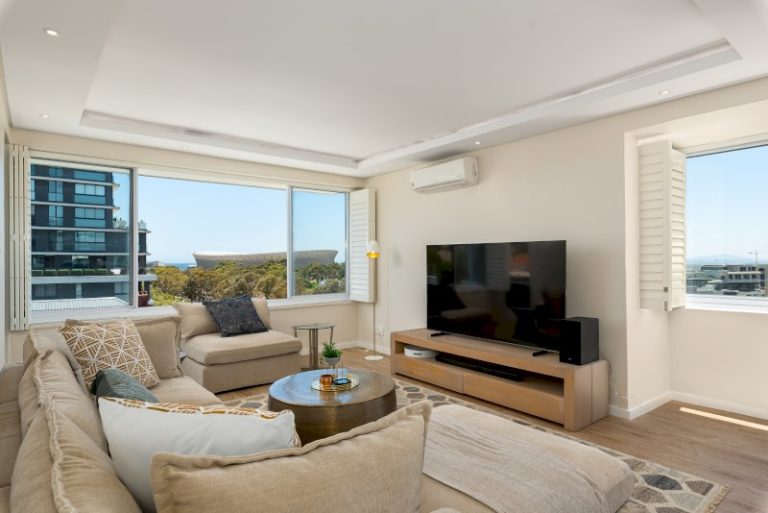 Modern open-plan lounge with stadium glimpses, abundant natural light, and comfortable contemporary furnishings for relaxed city living.