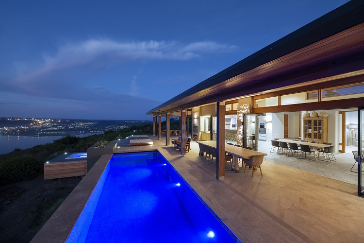 Alkira Lodge – Illuminated rim-flow swimming pool and expansive covered terrace overlooking the Knysna Lagoon, with seamless indoor-outdoor living and spectacular evening views.
