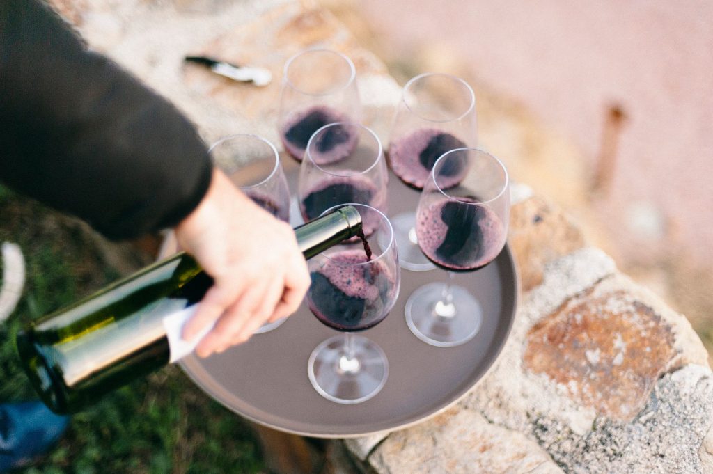 Close-up of red wine being poured into glasses on a tray, set outdoors.