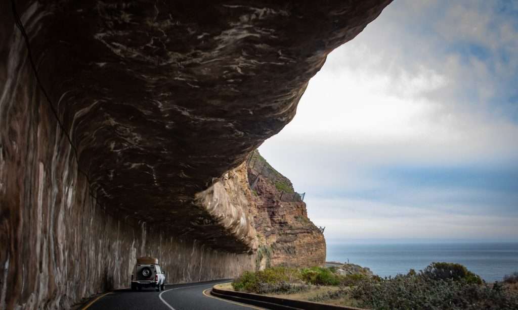 SUV driving along a coastal road beneath rocky cliffs in Cape Town