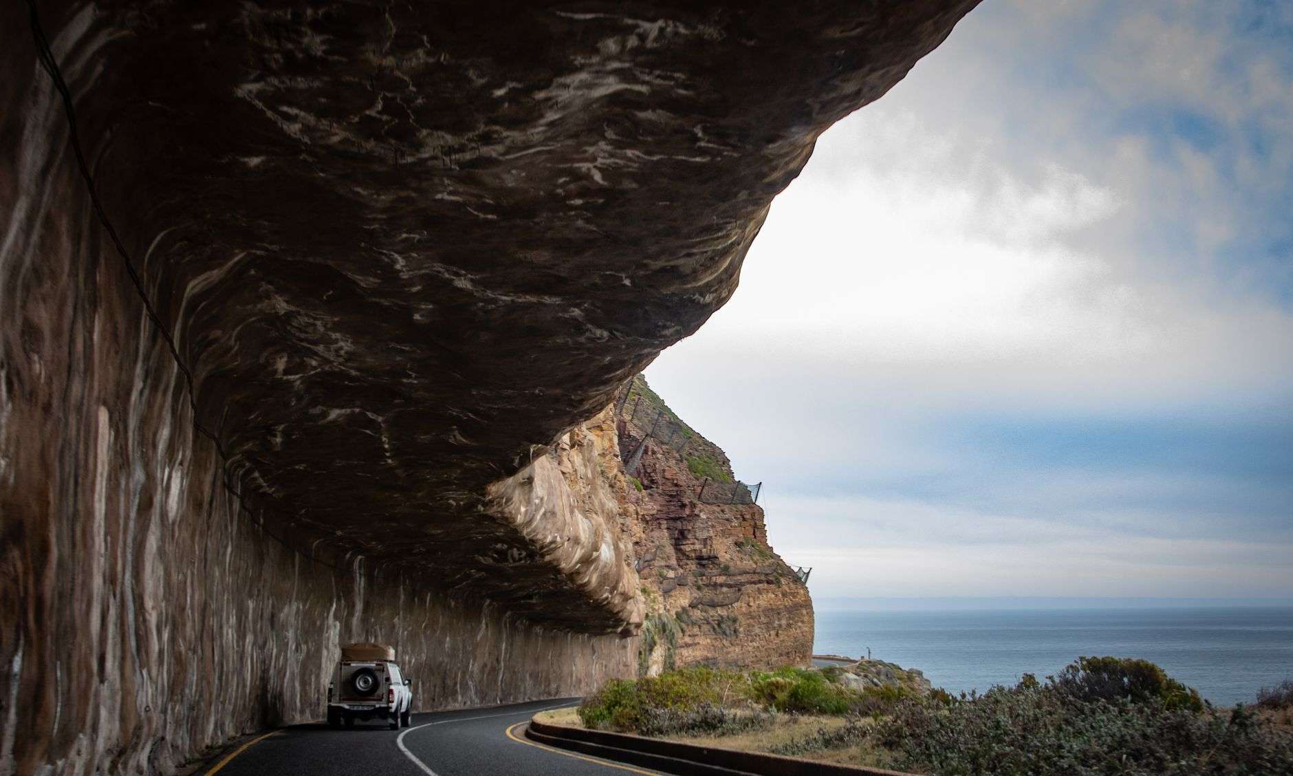 SUV driving along a coastal road beneath rocky cliffs in Cape Town