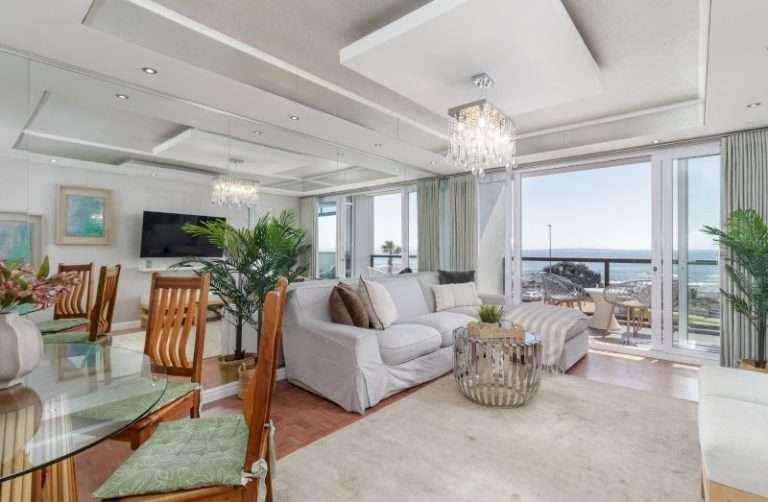 Mouille Point Seaside Stay – Living Area – Light-filled lounge and dining space with large windows and doors framing beautiful ocean views.