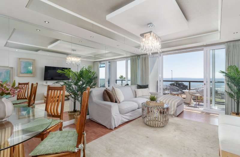 Mouille Point Seaside Stay – Living Area – Light-filled lounge and dining space with large windows and doors framing beautiful ocean views.