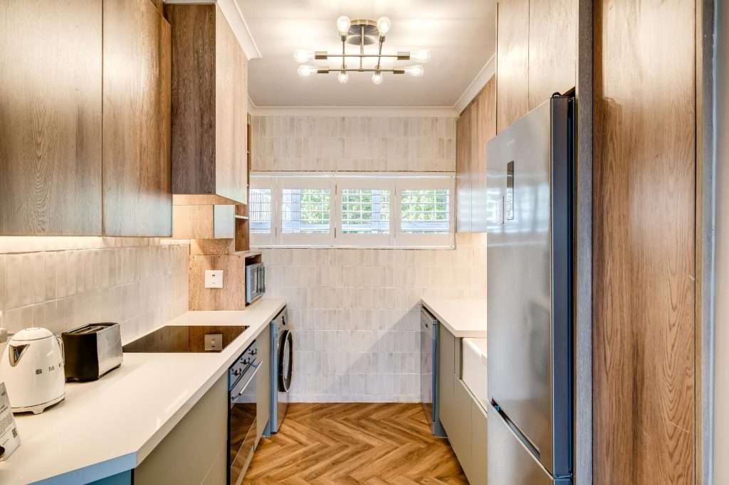 Shoreline Views – Kitchen – Sleek, fully equipped kitchen with warm wood cabinetry, modern appliances and elegant herringbone flooring.
