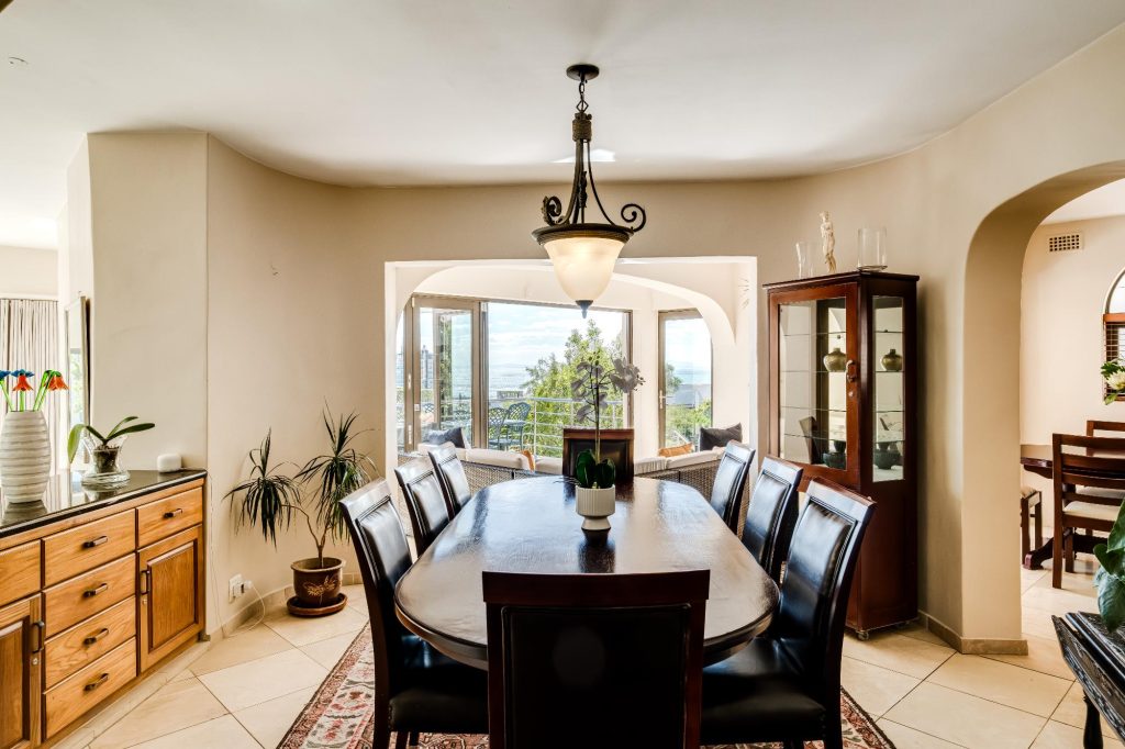 Kaya Eden – Elegant dining room with a large dark-wood table, classic furnishings and abundant natural light flowing in from the adjoining living space.