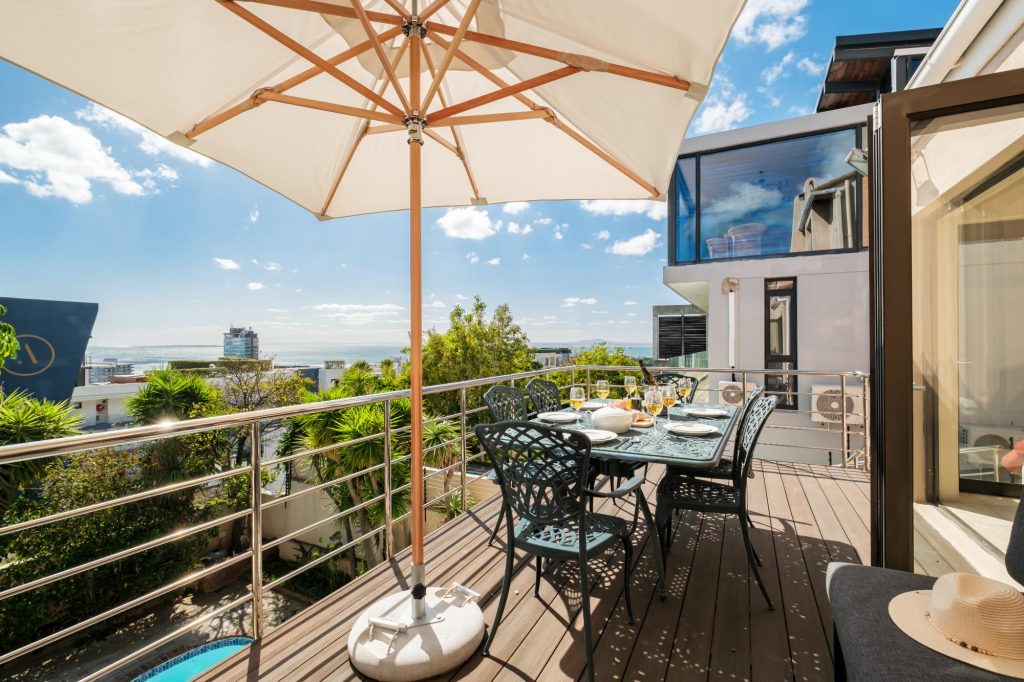 Kaya Eden – Spacious outdoor dining terrace with umbrella-shaded seating and beautiful ocean views, perfect for relaxed alfresco meals in the Cape Town sunshine.