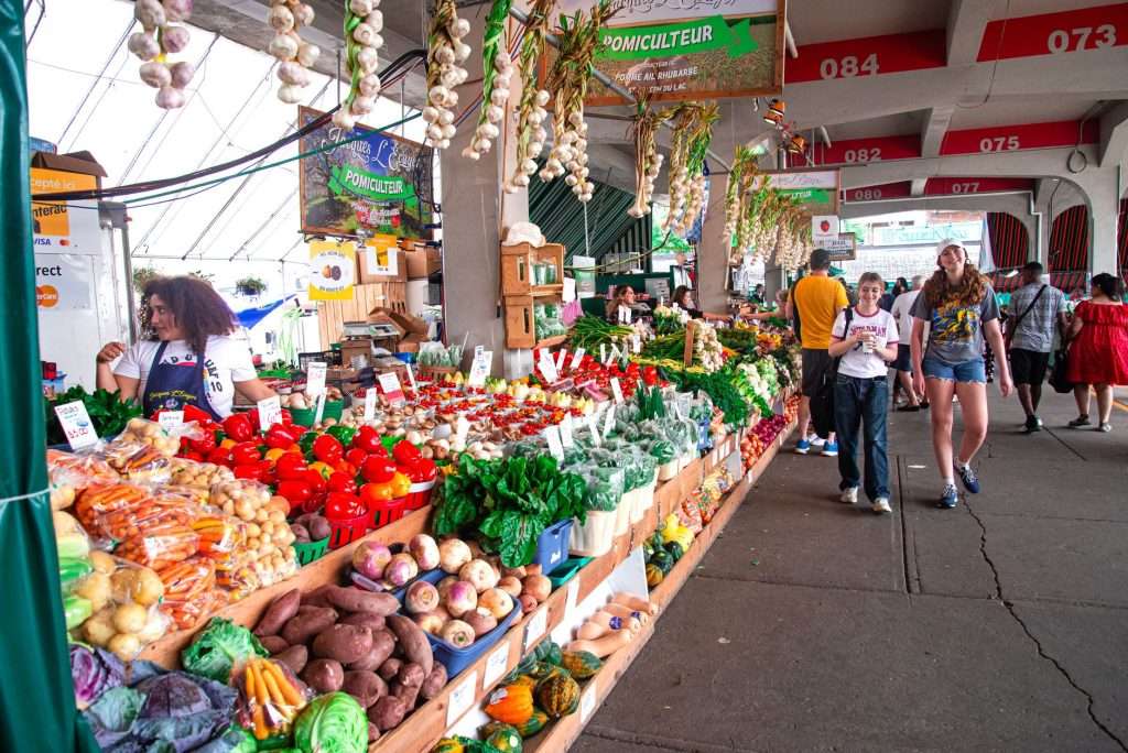 Colorful farmers market scene with shoppers exploring fresh produce stalls.
