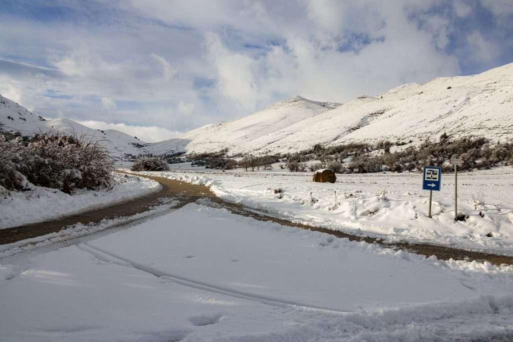 A snow-covered road with mountains and blue sky in winter, creating a serene and picturesque scene.