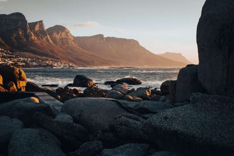 Cape Town’s rocky coastline at sunset with mountains in the background.