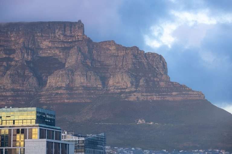 Scenic view of Table Mountain towering over Cape Town, captured at dawn with city buildings in the foreground.