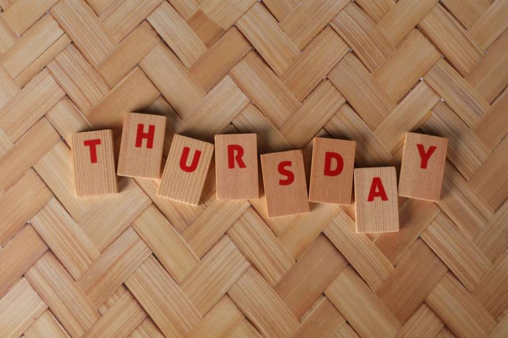 Thursday spelled out with wooden blocks on a woven pattern surface, offering a natural texture.