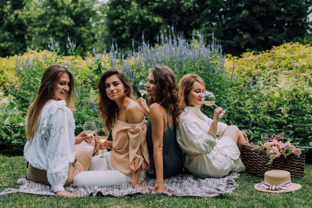 Two women enjoying a relaxing summer picnic in a lush garden setting.