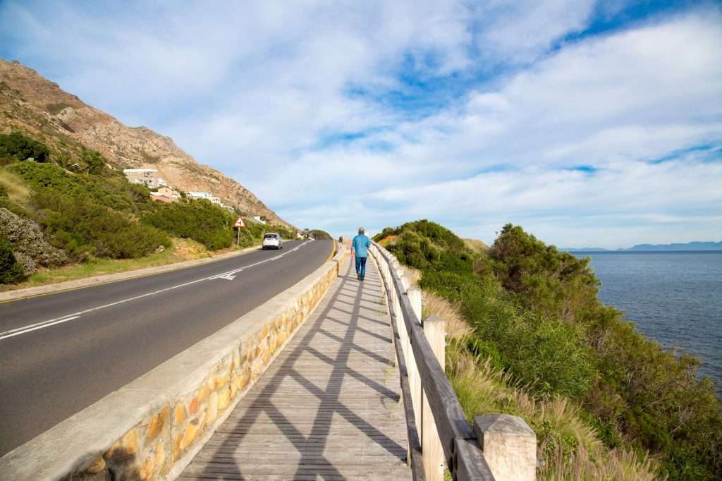 Person walking along a scenic Cape Town walkway with ocean and mountain views.