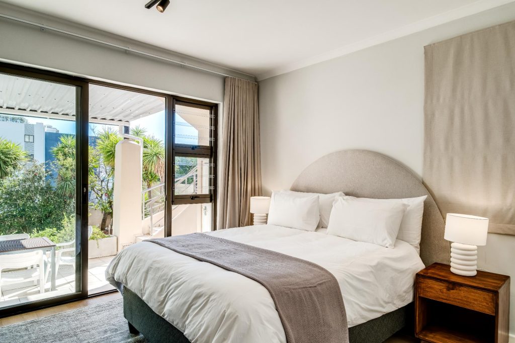 Kaya Eden – Light-filled double bedroom with a comfortable bed, contemporary upholstered headboard and glass doors leading onto a private outdoor area.