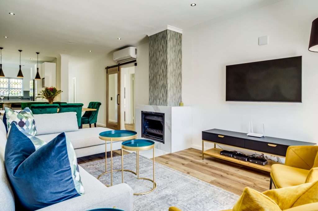 De Waterkant DW-001 – Lounge – Beautifully presented living room with generous seating, fireplace, large-screen television and stylish pops of colour.