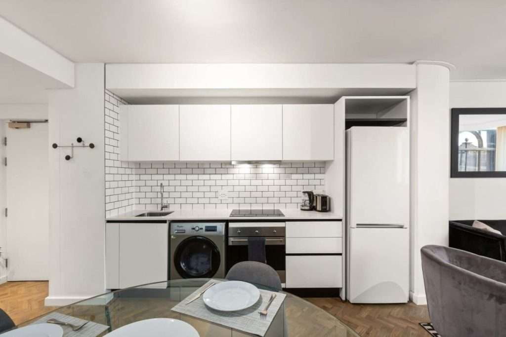 The Tuynhuys – Kitchen & Dining – Contemporary white kitchen with modern appliances alongside a glass dining table, ideal for easy self-catering meals.