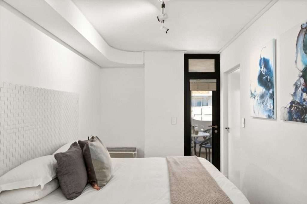 The Tuynhuys – Main Bedroom – Calm, beautifully presented bedroom with crisp white linen, soft neutral accents and contemporary artwork.