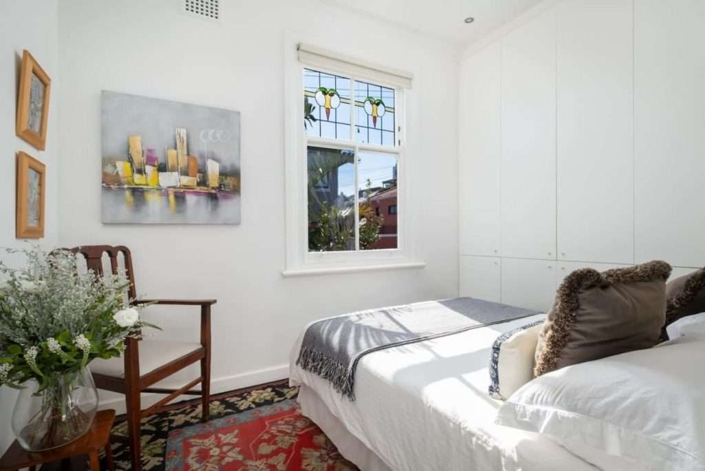 Timeless Sea Point Retreat – Second Bedroom – Bright and inviting bedroom with built-in cupboards, original stained-glass detailing and warm decorative touches.