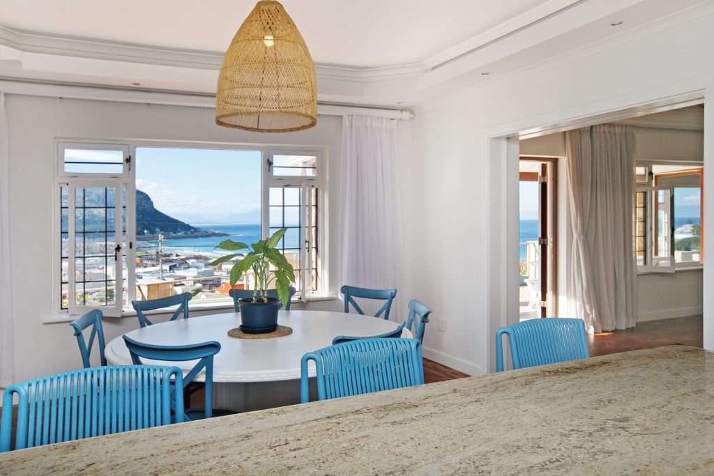 The Perch – Dining Area – Light-filled dining space with cheerful blue seating and wonderful elevated views across the village to False Bay.