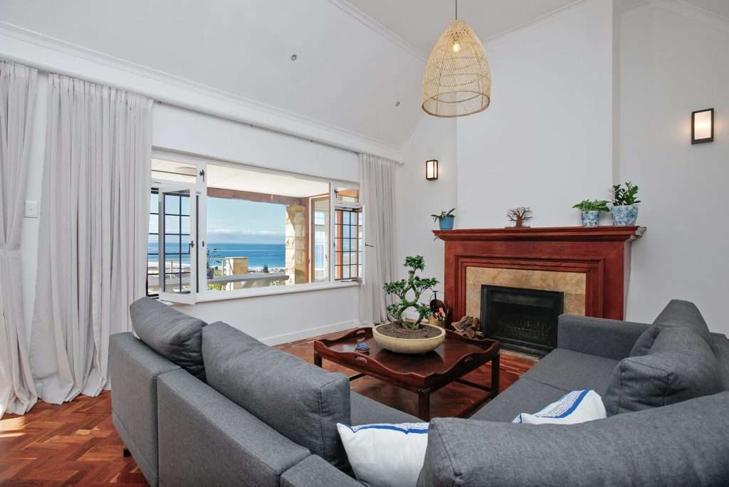 The Perch – Lounge – Comfortable living room centred around a fireplace, with large windows bringing in natural light and glimpses of the sea beyond.