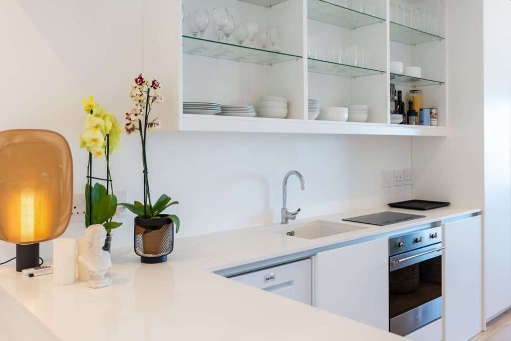 Mimosa Views – Sleek modern kitchen featuring white countertops, glass-fronted shelving, an electric hob, built-in oven and stylish contemporary finishes.