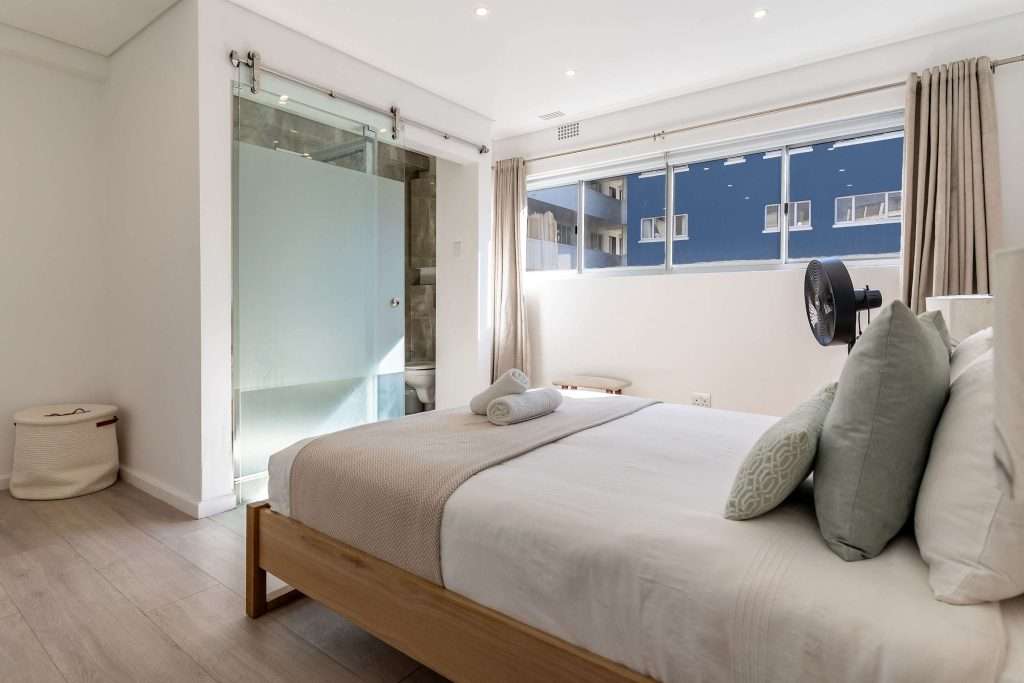 Protea Views Apartment – Bright bedroom with a comfortable double bed, soft green accents and a contemporary en-suite bathroom with a frosted glass sliding door.