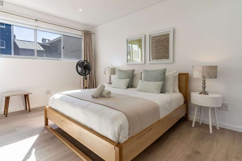 Protea Views Apartment – Inviting bedroom featuring a wooden bed frame, neutral furnishings, elegant bedside tables and large windows providing natural light.