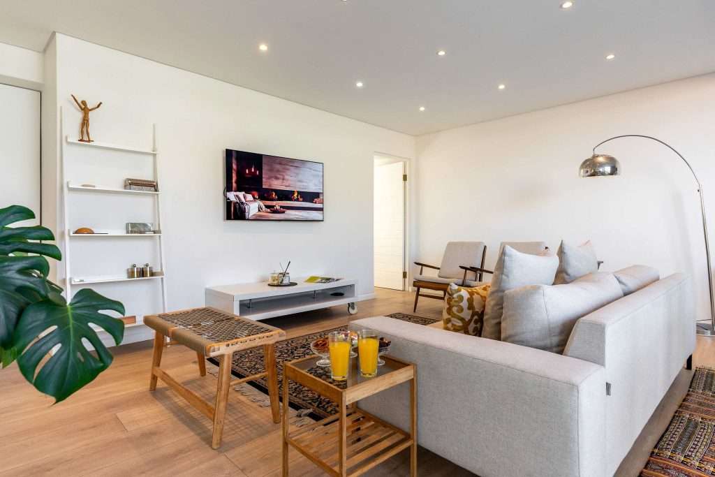 Protea Views Apartment – Stylish lounge with a comfortable sofa, wall-mounted television, modern furnishings and warm wooden flooring.