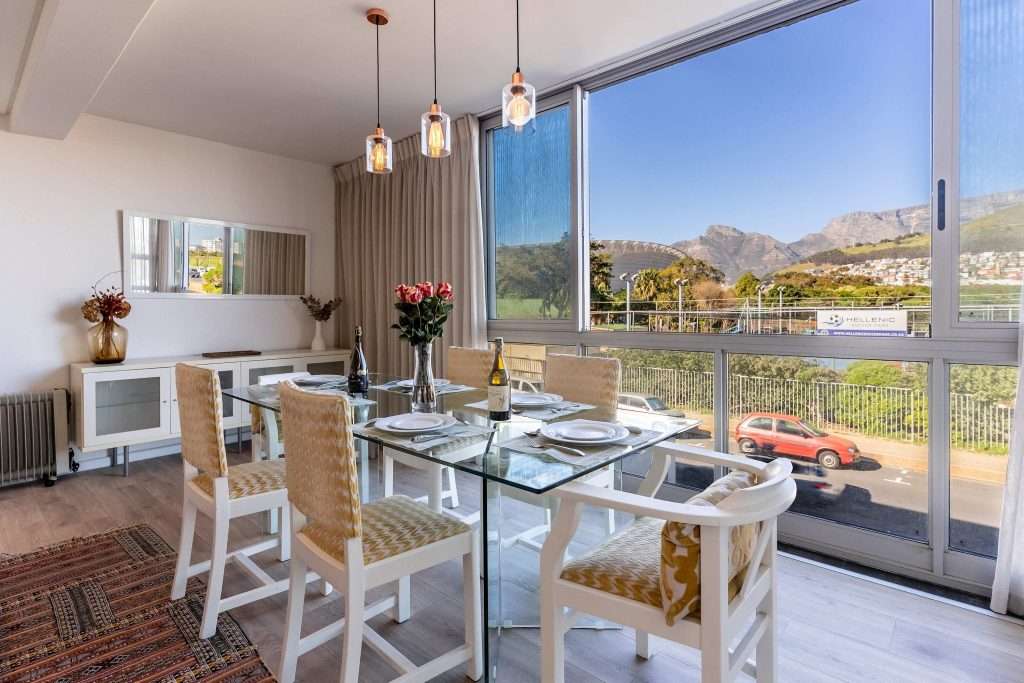Protea Views Apartment – Elegant dining area with a glass-top table, seating for six and large windows showcasing beautiful Table Mountain views.