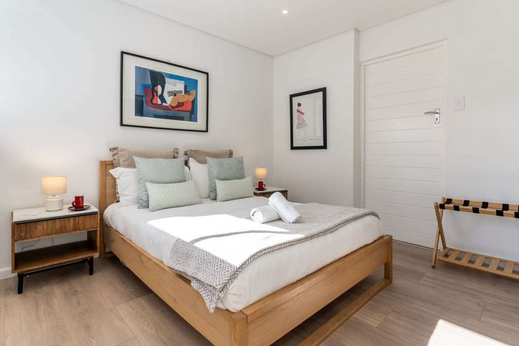 Protea Views Apartment – Peaceful bedroom featuring crisp white bedding, soft green cushions, contemporary artwork and warm bedside lighting.