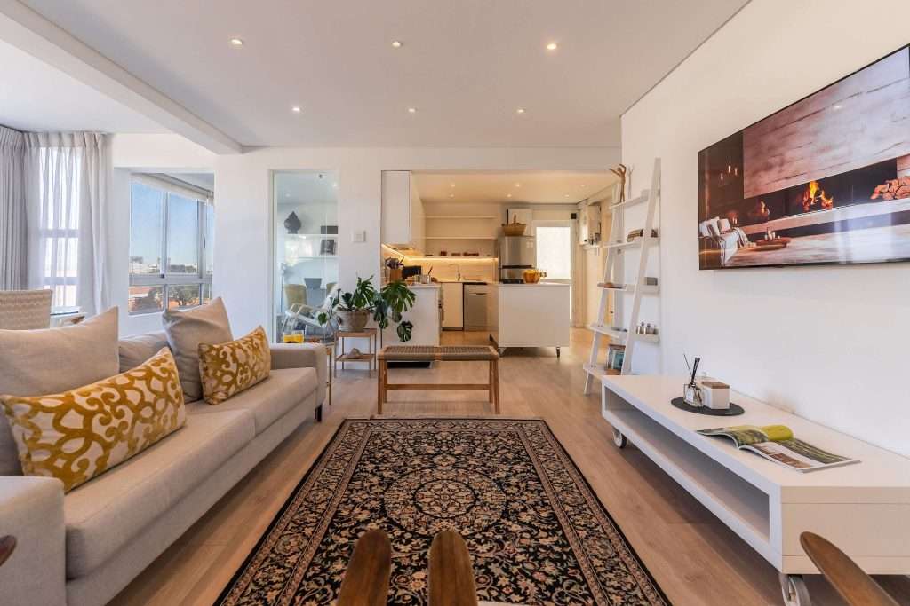 Protea Views Apartment – Spacious open-plan lounge with comfortable seating, a wall-mounted television, stylish décor and easy access to the modern kitchen.