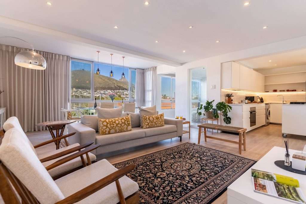 Protea Views Apartment – Light-filled living area with comfortable sofas, elegant armchairs and expansive windows framing beautiful mountain views.