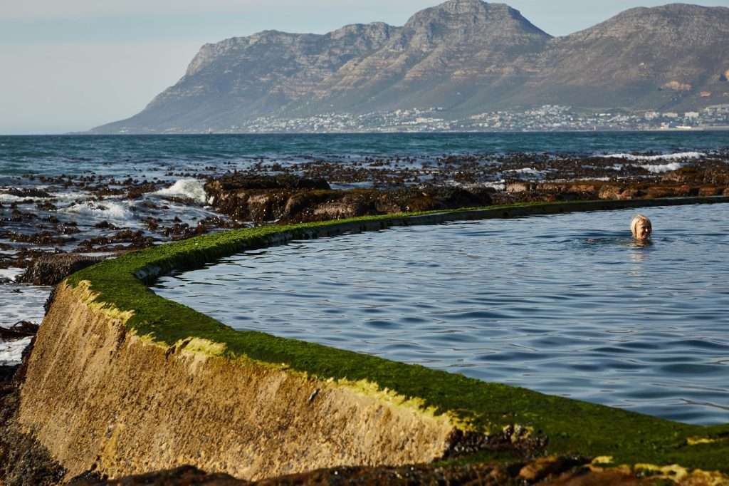 A serene scene of a woman swimming in a natural tidal pool with mountains in the background.